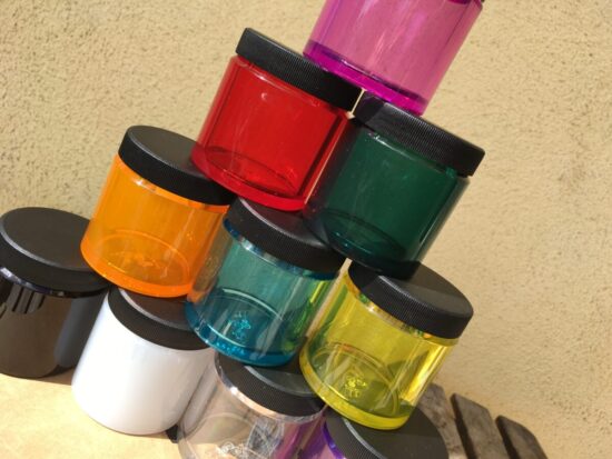 A stack of many colored polymer jars with screw top lids. They are stacked in a pyramid on the counter top.