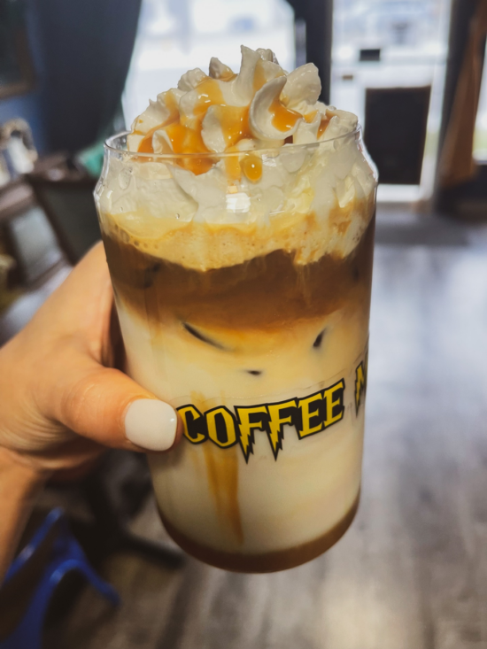 An iced horchata latte in a soda can-shaped glass, topped with whipped cream and caramel.