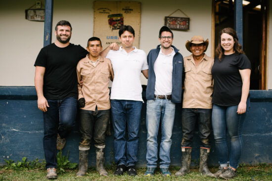Six people from Verve and Pergamino Team stand together, arms around each others' shoulders, in Urrao. Two wear rainboots and one wears a cowboy hat.
