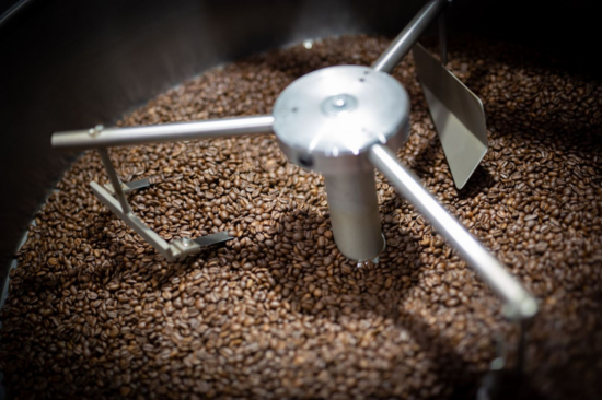 A view inside a coffee roaster, with beans already a medium roast, and three stainless steel arms on a wheel turning the beans.