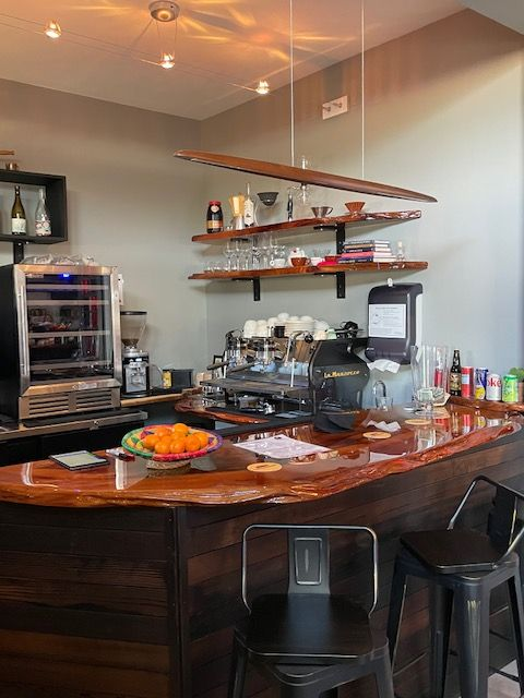 The coffee bar inside Rockaway Roastery. There are swivel bar chairs, a naturally shaped wood countertop and La Marzocco machine. A bowl of oranges sits on the counter.