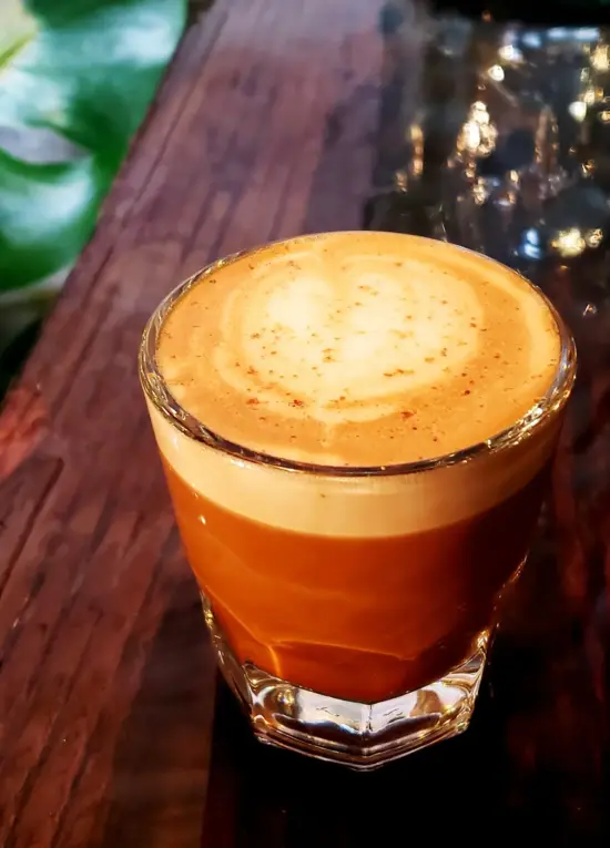 On a wooden bar, a rocks glass with a small coffee drink, which looks like a cortado.