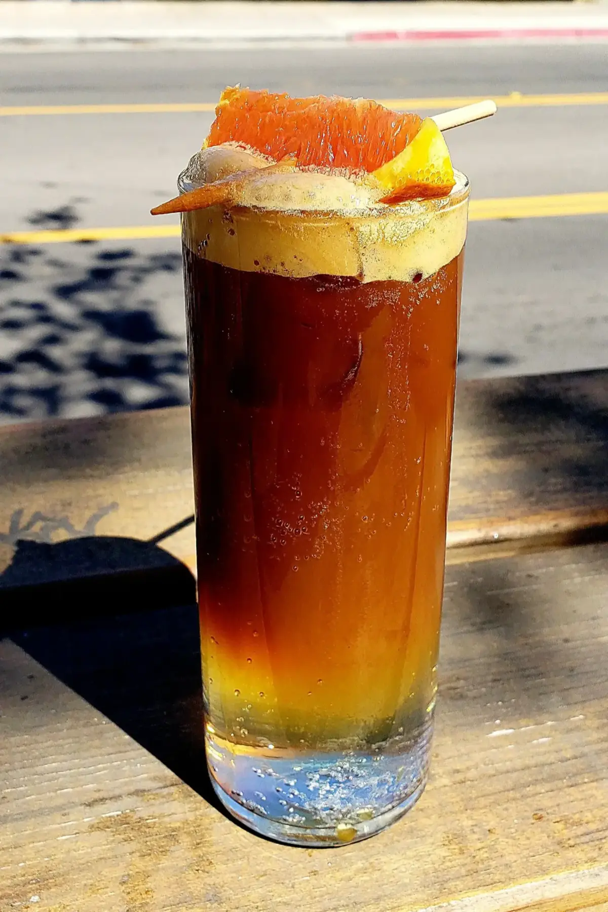 A tall glass with tonic and espresso bubbling at the top, and a skewered orange slice laid across the top of the glass.