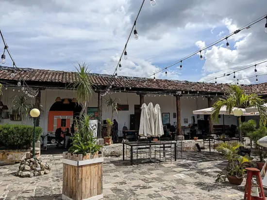 The patio at Coffee has paved stones, string lights, umbrellas over cafe tables and palm trees. The edges of the patio are covered by the outcropping tile roof.