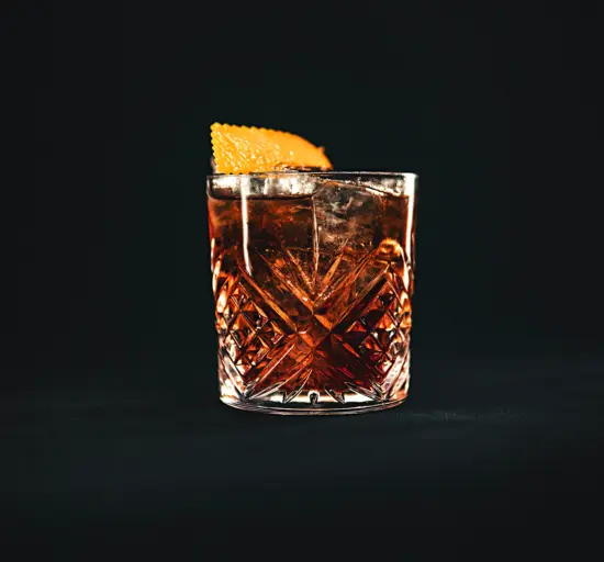 A faceted short glass with a brown liquid and orange peel.