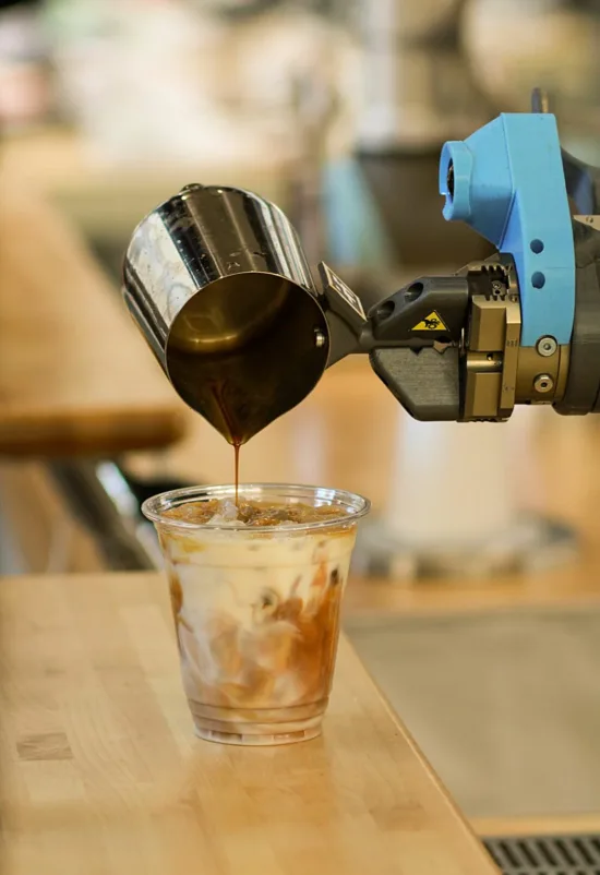 A blue arm empties an iced latte into a plastic cup.