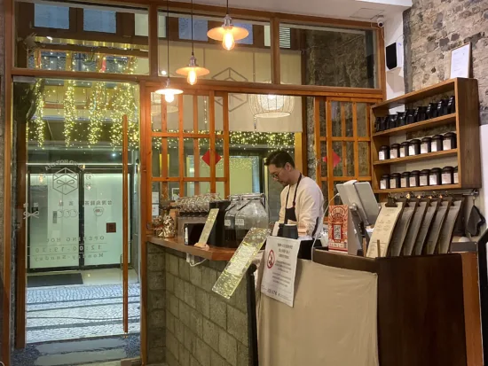 The host at Ho Ho Hot Cha behind the tea counter, which is stocked with jars and jars of tea and detailed menus.