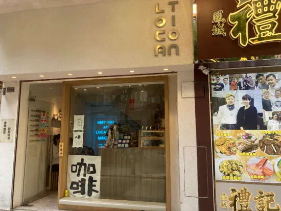 Outside Location Coffee's window, you can see the interior of the shop: neon blue sign, pastry case, espresso machine,