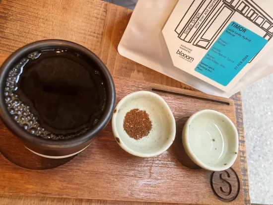 A pour over cup, coffee bag, and two small cups, one with coffee ground and one with hot water.