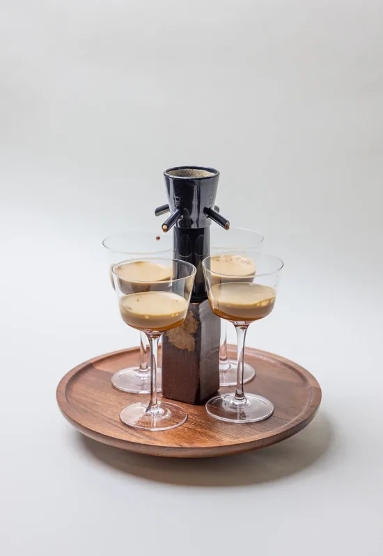 Four stemmed glasses are placed on a wooden tray, with a four-spout drink separator above.