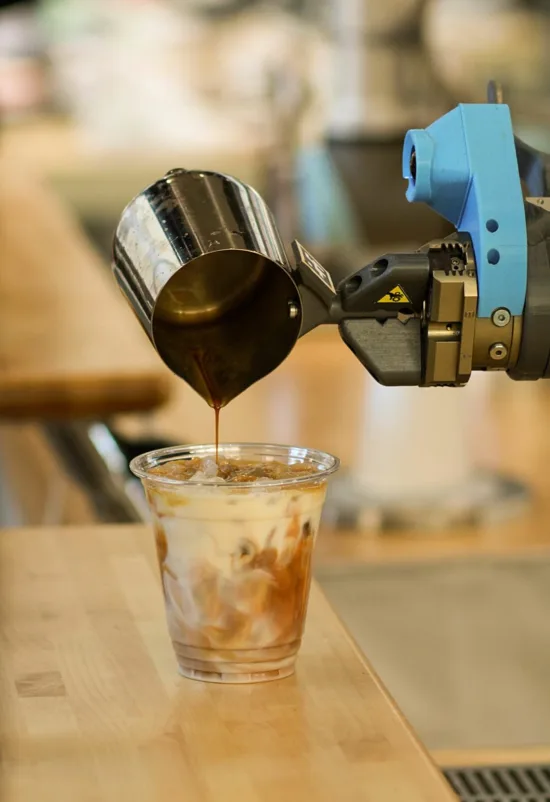 A robot arm pours espresso in a cold drink.