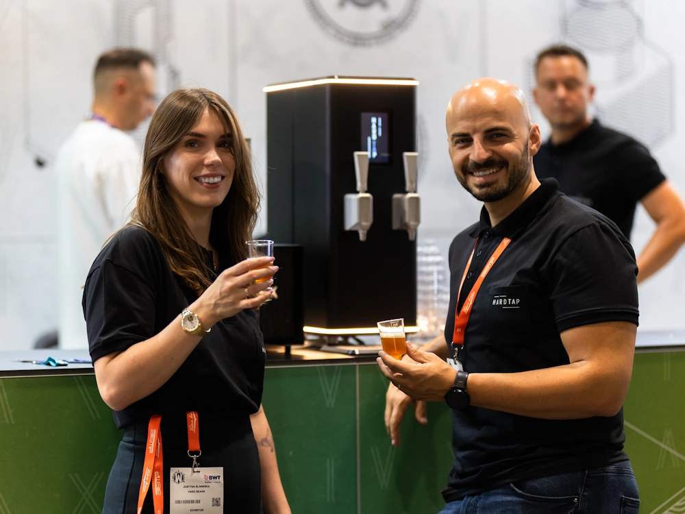 Two people sip drinks made using a Hardtap beverage dispenser at World of Coffee Geneva.