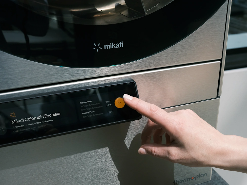 A person pushes a button on a Mikafi countertop roaster.